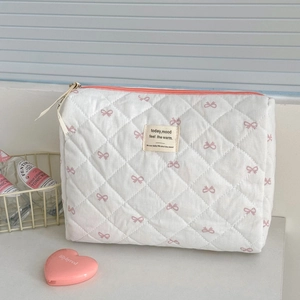 Détail de nœuds roses sur une trousse à maquillage blanche matelassée avec fermeture éclair