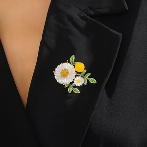 Broche marguerite avec pétales blancs, feuilles vertes et perle jaune sur un revers noir