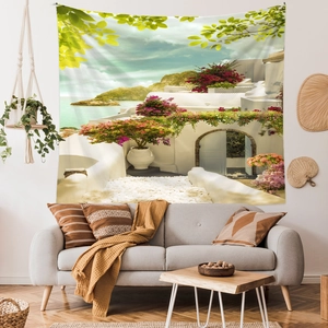 Santorini landscape wall tapestry hanging above a grey sofa in a cozy living room scene