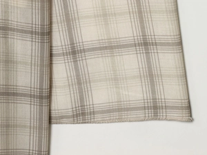 Detailed view of beige and white plaid woven fabric with clean overlock stitching hem