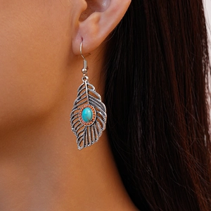 Close-up of bohemian feather earring with turquoise stone worn by a model