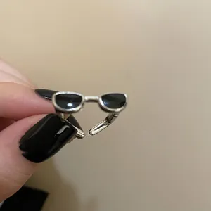 Détail d'une bague Y2K en forme de lunettes de soleil argentées avec émail noir réglable