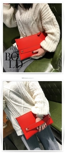 Detail van de rode envelop-clutch met goudkleurige hardware en een polsbandje
