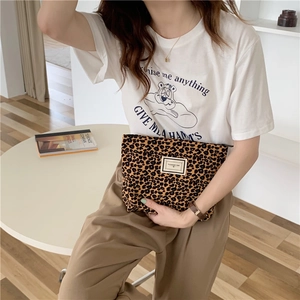 Detail of leopard print canvas makeup bag held by a model in a cozy indoor setting