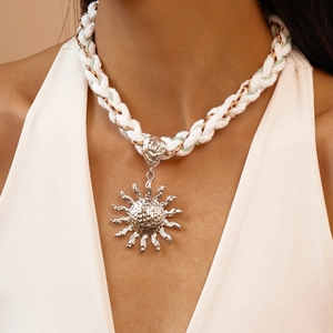 Macro view of silver sun pendant on white twisted cord necklace with metallic thread