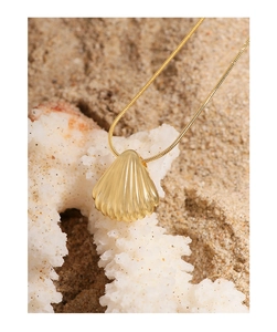 Detailed close-up of a gold shell pendant necklace displayed on white sea coral