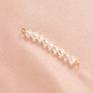 Detail of faceted rainbow crystal beads with gold wire connectors on pink fabric