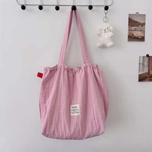 Pink striped drawstring tote bag with Sozakka brand label hanging on an ivory wall