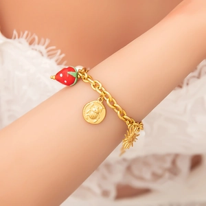 Detail of gold bracelet with red strawberry and beetle charms on a lace background