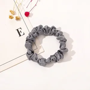 Close-up of grey satin scrunchie with soft fabric pleats and premium silk texture