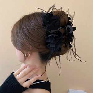 Detail view of a black ruffled fabric floral hair claw clip with delicate feather accents