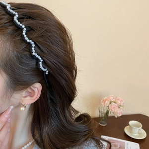 Close-up of wavy black headband with white pearls worn by a model in a warm setting