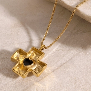 Detail of gold cross pendant with black heart on twisted chain and hammered texture
