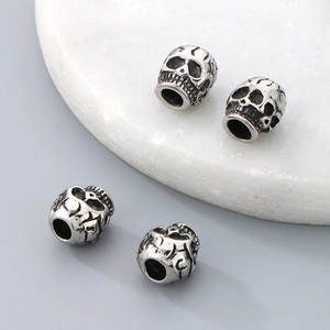 Detailed view of vintage silver skull beads for DIY jewelry making on marble surface