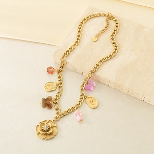 Detail showing a gold stainless steel necklace with flower and butterfly charms on a stone