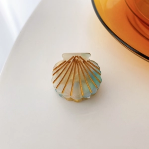 Close-up of shell-shaped acetate hair claw with pearlescent finish and gold accents