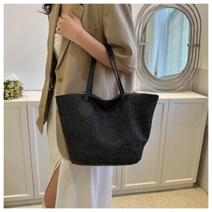 Detailed view of black woven straw tote bag with long thin shoulder straps and leather patches