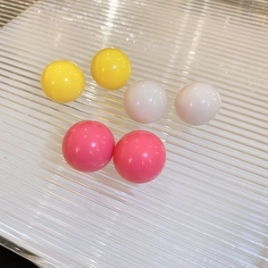 Detail of candy-colored spherical stud earrings in yellow, cream, and rose red resin