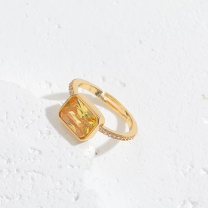 Gold open ring with a large rectangular yellow gemstone and zircon accents on stone background