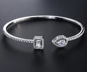 Detail of silver open bangle featuring pear and emerald cut zircon stones in a halo setting