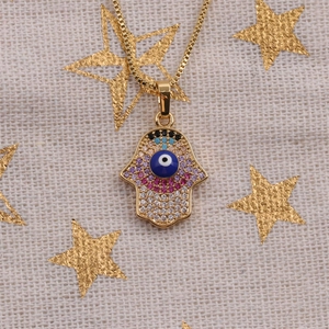 Gold Hamsa Hand necklace with colorful zircons and blue evil eye on white fabric