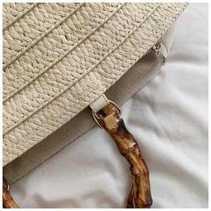 Detail of straw tote bag with brown bamboo handles and secure silver zipper closure