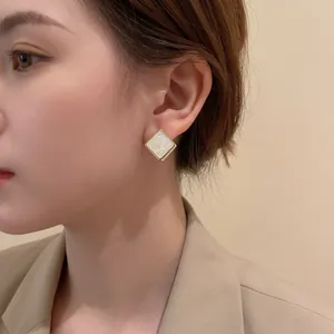 Boucles d'oreilles carrées dorées avec nacre portées par un mannequin chic