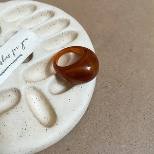 Close-up of amber resin oval ring on a textured ceramic tray with warm lighting