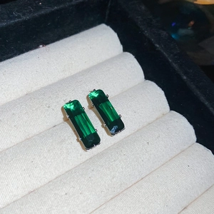 Macro shot of emerald green rectangular zircon earrings in a beige fabric jewelry box