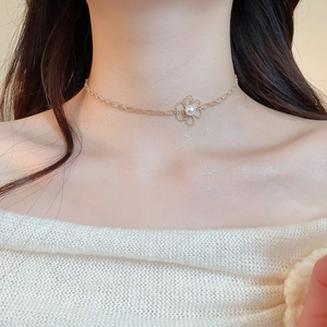 Close-up of golden hollow flower pendant with center pearl on a delicate necklace chain