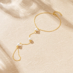 Detail of a gold slave bracelet with white pearls on a soft beige textured background