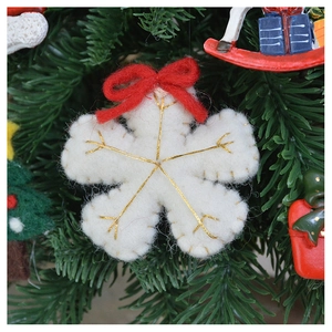 Close-up of white felt snowflake ornament with red bow on green Christmas tree branch