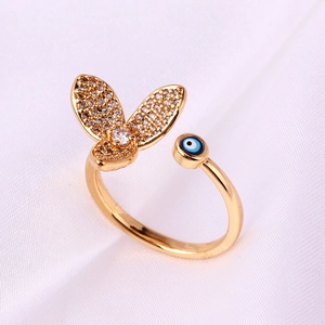 Detail of gold evil eye and crystal butterfly open ring on white textured fabric