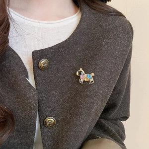 Detailed close-up of a pink and blue crystal horse brooch on a tweed blazer coat