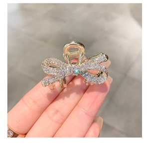 Close-up of a small golden bow hair claw clip with sparkling rhinestones and crystal