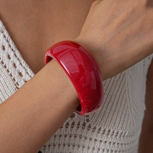 Detail view of bold red acrylic bangle on a model showing glossy finish and wide design
