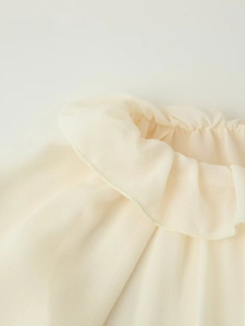 Dettaglio del top in chiffon beige chiaro con scollo a balze e trama morbida e traspirante