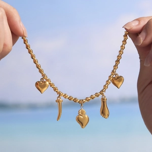 Goldenes Bambus-Gliederarmband mit Herzanhängern vor einem sonnigen Strandhintergrund