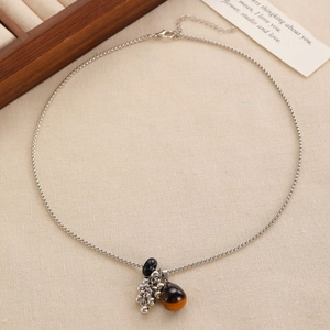 Detail of beaded necklace with amber teardrop and silver clusters on beige fabric