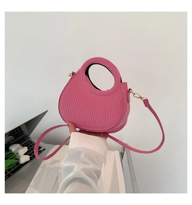 Close-up of pleated rose pink saddle bag with integrated circular handle and gold hardware