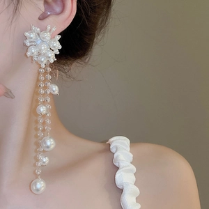 Detailed close-up of floral pearl earrings with long crystal tassels on a model