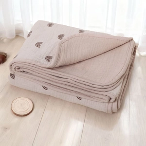Detailed view of folded cotton gauze baby blanket with rainbow pattern on wooden floor