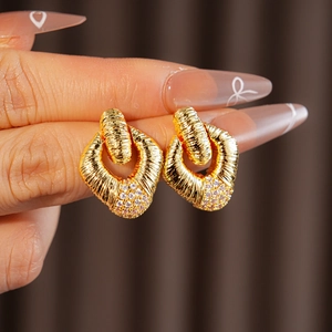 Detail of golden textured rhombus earring with pink gemstone inlay held by fingers