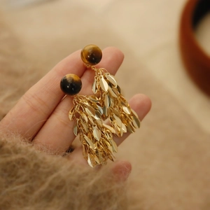 Detailed close-up of golden leaf tassels and brown resin bead earrings in hand