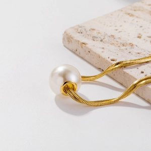 Detailed close-up of a single white pearl pendant on a gold snake chain over stone