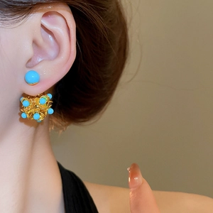 Detailed view of teal beaded flower earrings in gold setting worn by a female model