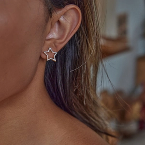 Close-up of a gold star-shaped earring with small clear crystals on a female model