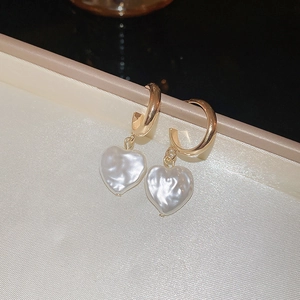 Dettaglio di perle a forma di cuore su orecchini a cerchio dorati su sfondo di seta