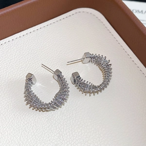 Macro shot of twisted silver-tone C-shaped earrings with spiral texture on beige leather