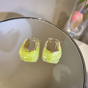 Macro shot of neon yellow U-shaped acrylic earrings on a mirror with golden accents